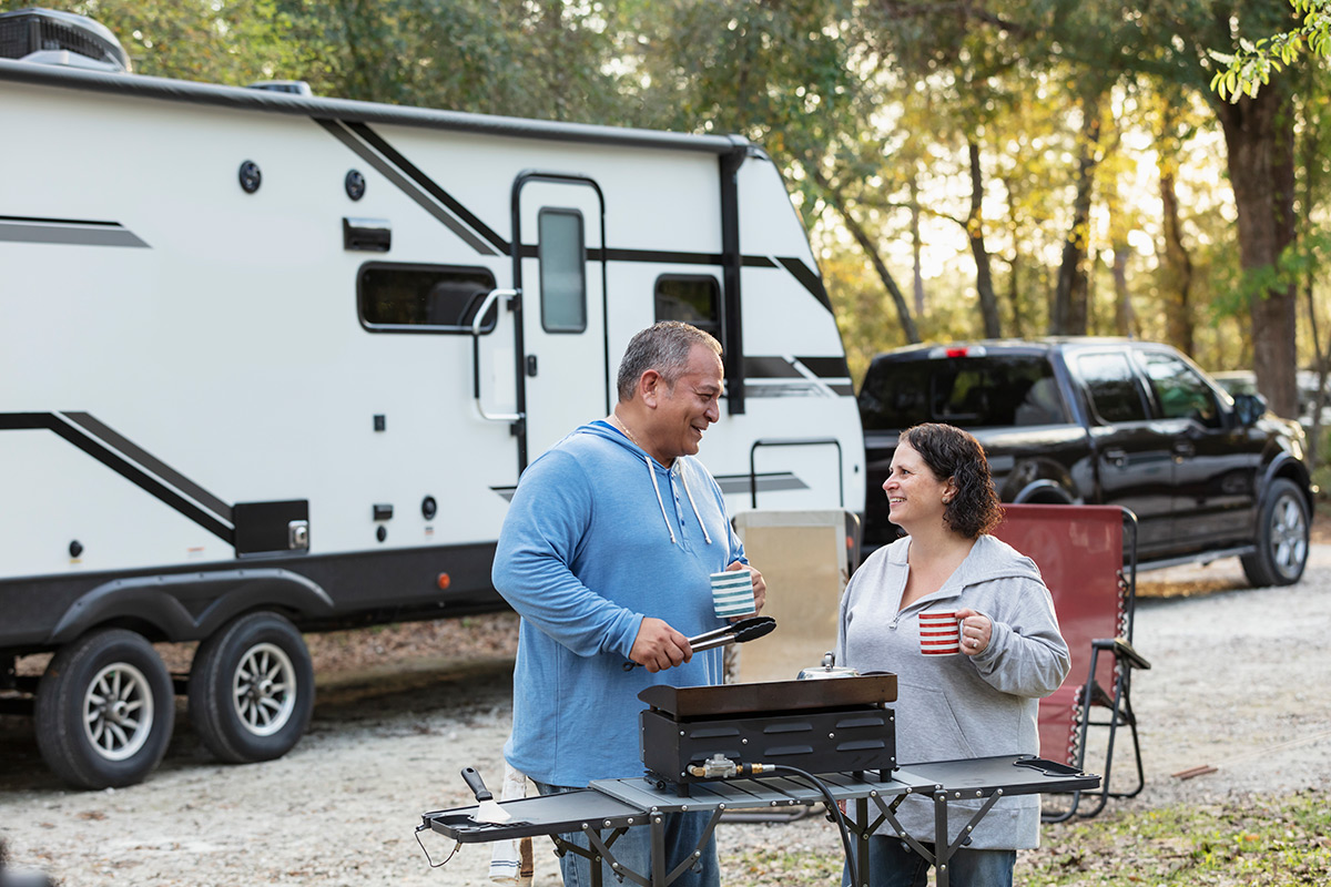 A couple enjoy a barbecue in front of their caravan.