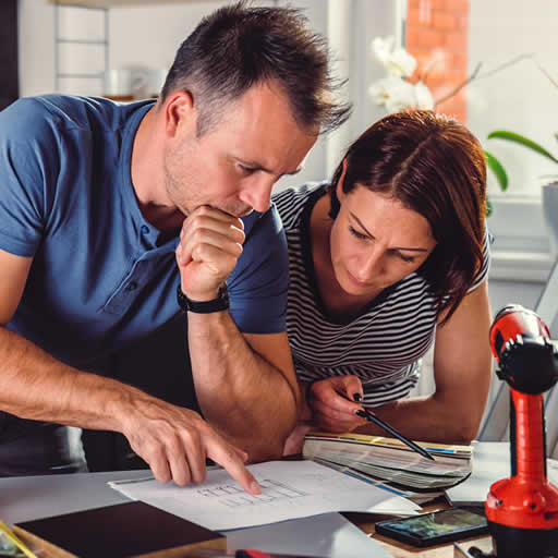 Couple studying home improvement plans with power drill in foreground.