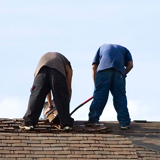 Two men in casual clothes trying to repair a tiled roof.