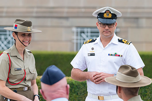 Military personnel standing in uniform, speaking with others who are seated.