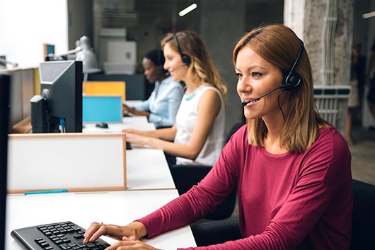 Smiling call centre staff talking through headsets at their desks.