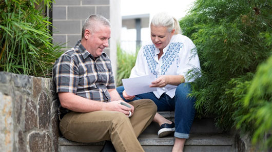 Older couple sitting on steps reading document.