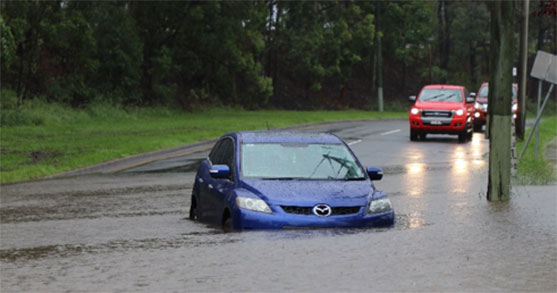 Car partially submerged in floodwaters with other cars behind.