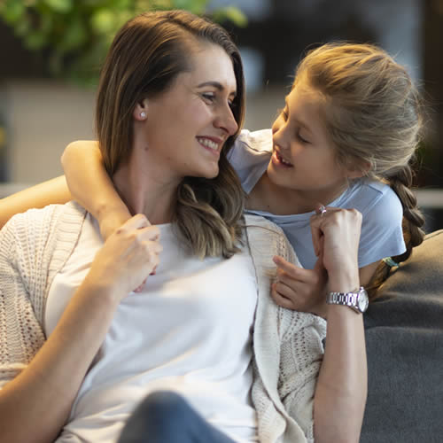 Mother and daughter smiling at each other while girl puts her arm around her mother.