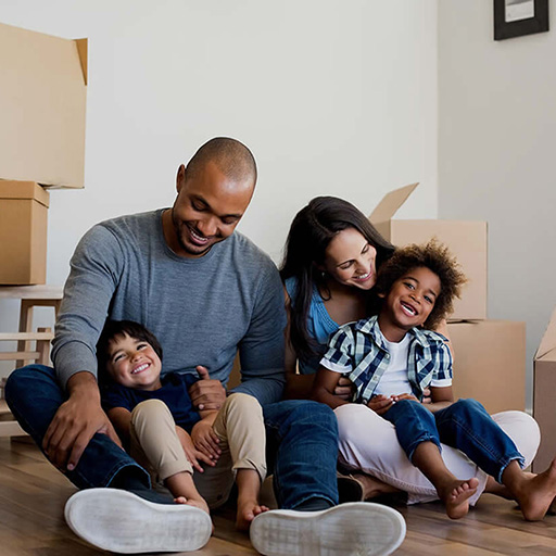 Young boys sitting on their parents' laps on floor surrounded by moving boxes.