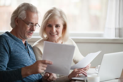 Retired couple look at paperwork with laptop in foreground.