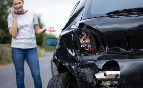 Woman on phone standing beside car damaged in a road accident.