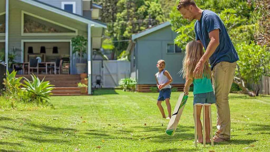 Father playing cricket with children in yard of beachfront home.