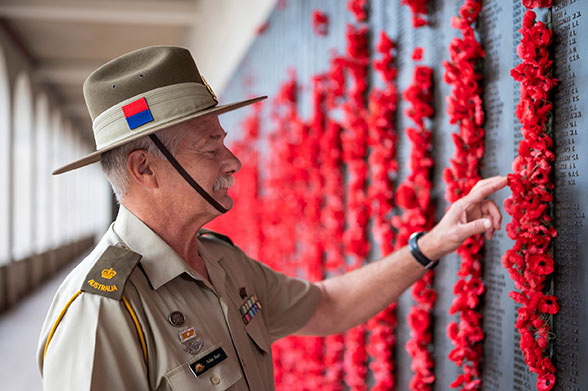 An older veteran in uniform reading names on the wall of remembrance.