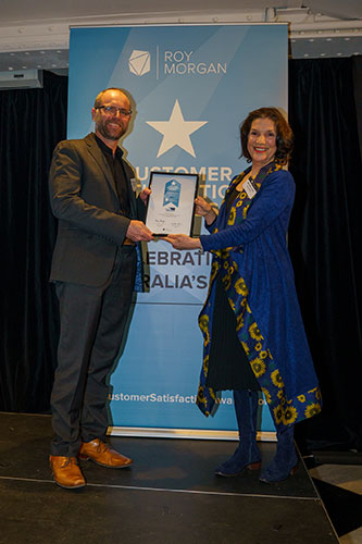 A man and woman holding together the framed award certificate.